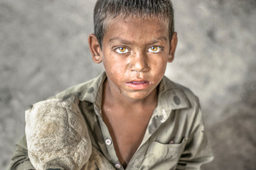 closeup of a poor staring hungry orphan boy in a refugee camp with sad expression on his face and...
