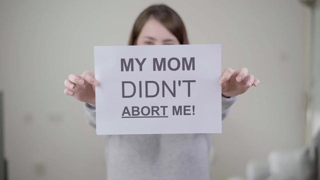 Woman holding a paper with the phrase "My mom didn't abort me".
