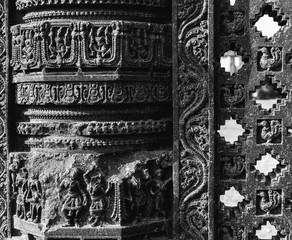 A black and white shot of the faded artwork and ornamental details on an ancient, ruined stone pillar in the archaeological site of the Warangal Fort.