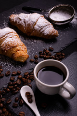 cup of black coffee and croissant on a dark background
