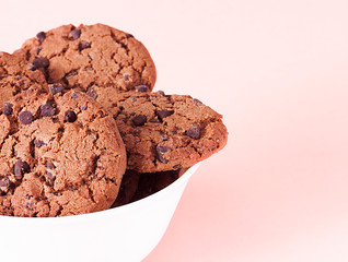 Chocolate chip cookies in white bowl on light pink background