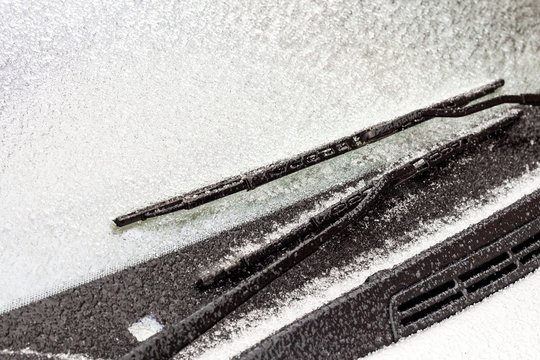 Frozen car wipers. Dangerous ice on the road. Frost on the windshield of the car. Detail of a frozen car window. Danger in transport.