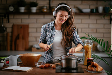 Young woman in kitchen. Beautiful woman singing and dancing while cooking. Woman listening music...