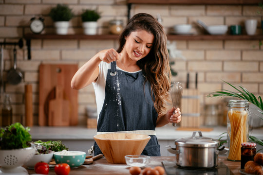 Young woman in kitchen. Beautiful woman having fun while making  dough. - Powered by Adobe