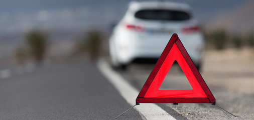 Broken down car with warning triangle behind it waiting for assistance to arrive, red triangle of a car on the road