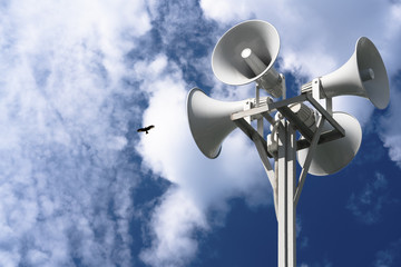 Four loudspeakers are attached to a rack against a background of clouds and a bird.
