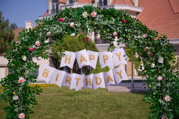 Arch decor . Birthday arch decorated . Happy Birthday texts. Woven plants forming an arch in beautiful garden . decorated flower . Birthday arch indoors. Festive decorations with colorfull flowers .