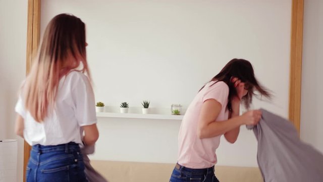 Teen girls fun. Home leisure. Two happy sisters having pillow fight on bed at home.