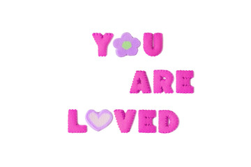The word YOU ARE LOVED spelled with vivid pink alphabet cookies and purple marshmallow on white background