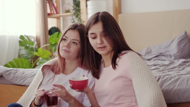Friends bonding. Home leisure. Two teen girls drinking tea enjoying watching movie together.