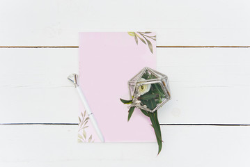 Blank pink sheet for text on a white wooden background, next to a pen and a box of flowers