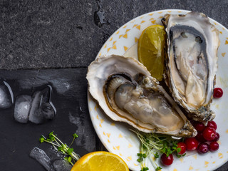 Oysters heart shape in plate with lemon, cranberries, microgreens, knife, shells on marble.