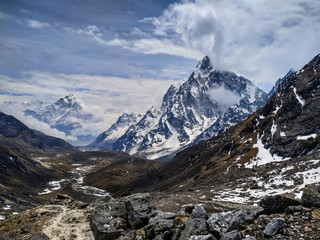 Cholatse and Taboche mountain peaks rises above valley near Cho La pass in Sagarmatha national park in Himalayas in cloudy day. Blurred Ama Dablam mountain is visible in the background.