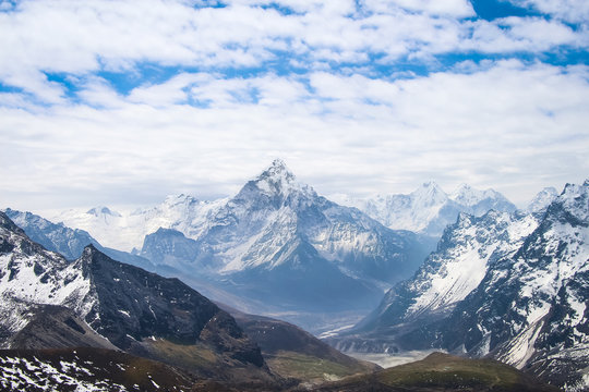 Ama Dablam mountain rises above valley in cloudy day near Cho La pass in Sagarmatha national park in Himalayas. Ghola Tsho lake is visible at the foot  of mountain.