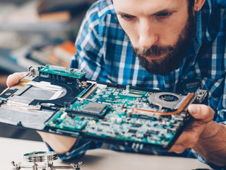 Hardware diagnostics. Disassembled laptop. Technician studying computer motherboard.