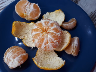  close-up of peeled ripe orange tangerine fruit, spread slices and peel lie on the surface of a blue plate