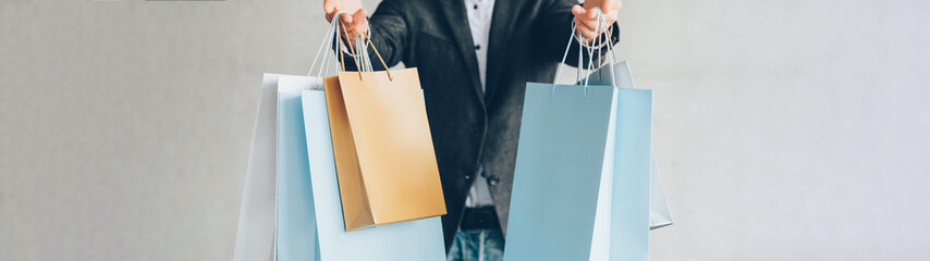 Black Friday shopping. Sale promotion. Man holding mockup brand bags on gray background.