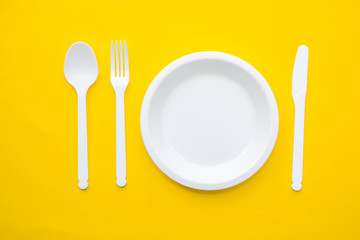 Plastic white fork, knife, spoon and plate on yellow background. Cooking utensil. Top view. Minimalist Style. Copy, empty space for text