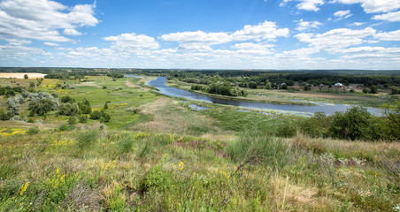 View on a river in a bright summer day. Picturesque countryside landscape. Green grass, cloudy sky.