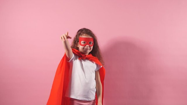 Spaceman concept. Little girl wearing red cloak and mask on eyes stand isolated over pink background.