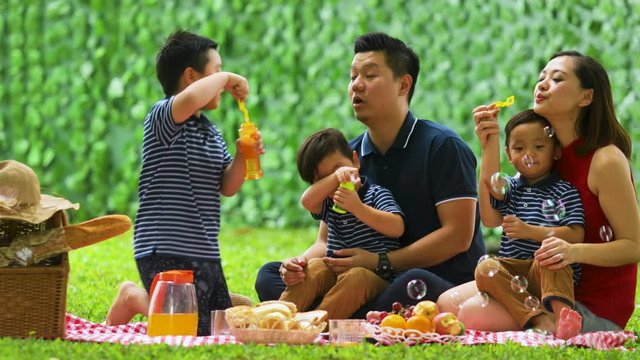 Asian family blowing soap bubble while picnicking