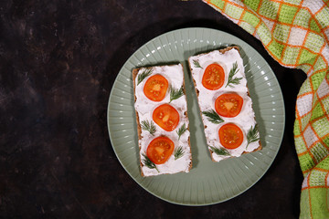 Crispbread with curd cheese and cherry tomato lies on a plate, on a dark background. Space for text. Flat lay, top view. Diet snack.