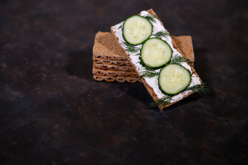crispbread with curd cheese and fresh cucumber on a dark background. Space for text. Flat lay, top...