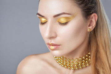 Portrait of a beautiful happy woman with beautiful creative makeup in gold colors. She has gold beads on her neck, in her hands and gold earrings. Make-up concept.