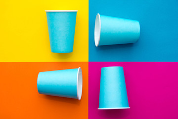 Blue paper disposable cups on beautiful multicolored background. Top view. Minimalist Style. Copy, empty space for text