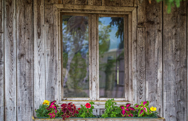 Fototapeta na wymiar Window of a wooden cottage with decorative flowers on windowsill.