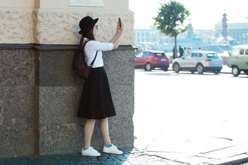 Tourist in the city takes a photo on smartphone. A young woman in a black hat and a white shirt,