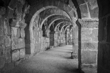 A black and white photo of old ancient building corridor, made of stone columns and arches