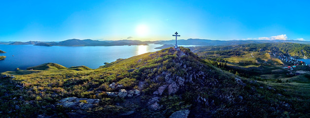 Beautiful futuristic panoramic aerial drone view to summer recreation facilities on the banks of the Bukhtarma reservoir on the Irtysh river with an Orthodox cross on top of mountain, East Kazakhstan