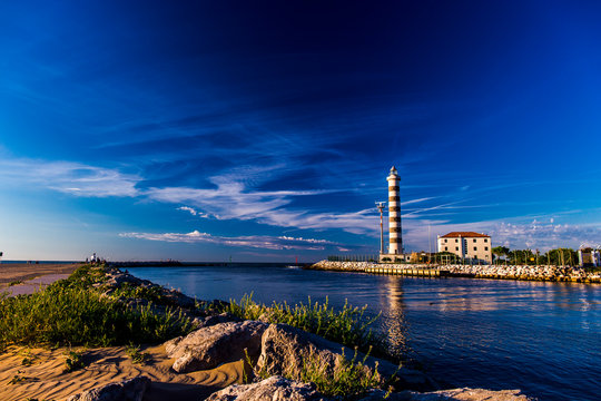 View at the lighthouse in the bay with beach on the other side and beautiful blue sky. Sunrise time. Jesolo, Italy.