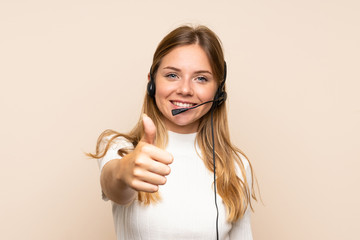 Young blonde woman over isolated background working with headset with thumb up