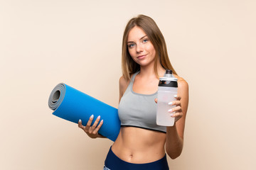 Young blonde sport girl over isolated background with sports water bottle and with a mat