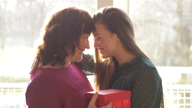 Loving adult daughter presenting spring flowers to happy old mother laughing bonding embracing, young woman congratulating hugging middle aged mom. Mothers day at home