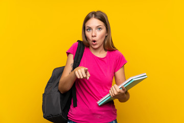 Young student girl over isolated yellow background surprised and pointing front