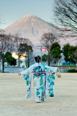 Japanese teenager wearing traditional kimono with arms outstretched contemplating the beauty of Mt. Fuji celebrating the Coming of Age Day in Fuji City, Japan. Vertical shot.