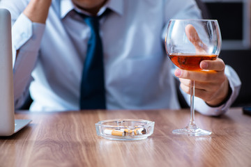 Male employee drinking alcohol and smoking cigarettes at workpla