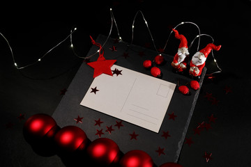 Christmas greeting card on a black stand with a red star, decorated with red Christmas balls, berries, garland and two toys of Santa Claus.