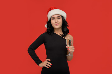 Beautiful brunette girl in a black dress and Santa hat holding glass of champagne.