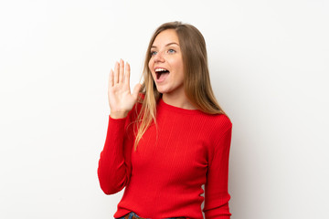 Young blonde woman with red sweater over isolated white background shouting with mouth wide open