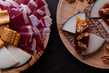 Variety of wood plates with freshly jamon, cheese and roasted bread; a whole cheese and toasted bread with cheese, nuts and quince jelly.