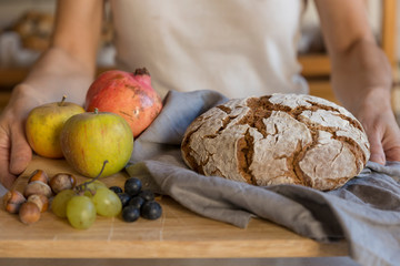 Woman holding a wooden tray with bread and fruits