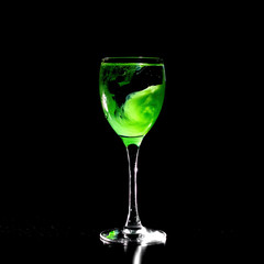 Glass on black background with bizarre pattern of green paint blurred in water. Odd drink, water witch, witchcraft.
