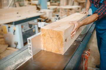 Carpenter processes wooden beam on plane machine