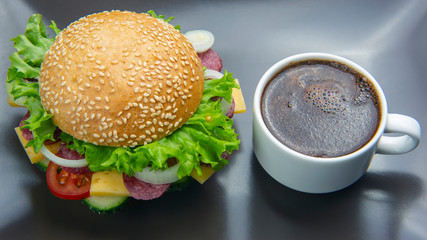 Hamburger with vegetables and sausage and coffee on a gray background. Fast food and breakfast. Calories and diet.
