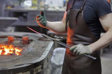 Worker in the blacksmith shop shows tongs with forged preheated workpiece