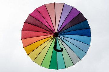 Large rainbow opened textile umbrella viewed from below towards white background 